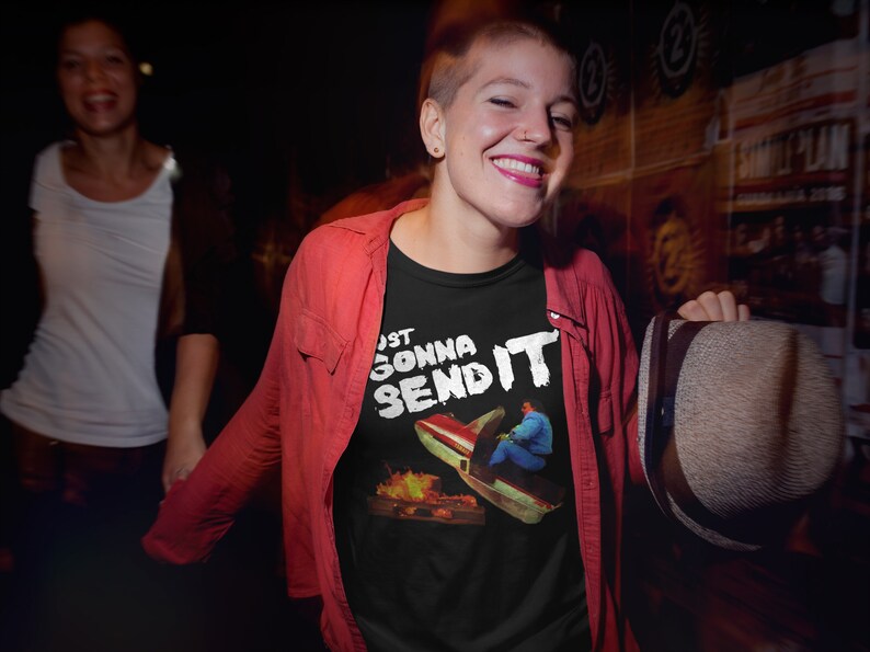 K&ouml;nnte beinhalten: Ein schwarzes T-Shirt mit einem wei&szlig;en Aufdruck einer Person, die ein Auto von einer Rampe mit Flammen f&auml;hrt, und dem Text "Just Gonna Send It".