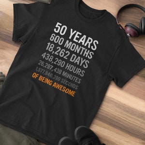 May include: Black t-shirt with white text that reads "50 Years 600 Months 18,262 Days 438,290 Hours 26,297,438 Minutes 1,577,846,299 Seconds of Being Awesome".