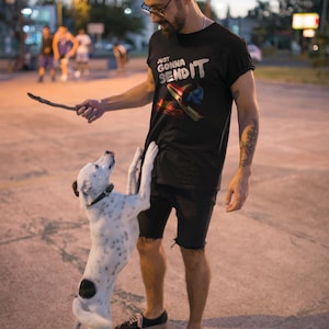 K&ouml;nnte beinhalten: Ein Mann tr&auml;gt ein schwarzes T-Shirt mit dem Text "Just Gonna Send It" und einem wei&szlig;en und blauen Grafikdesign. Er steht mit einem Hund da, und beide schauen auf einen Stock auf dem Boden.
