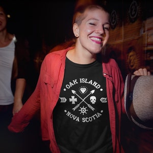 May include: A black t-shirt with a white graphic design featuring the text "Oak Island, Nova Scotia" and a compass, skull, cross, and diamond.
