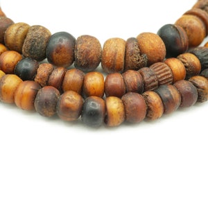 May include: A close-up of a brown wooden beaded necklace with dark brown and black beads. The necklace is made of natural wood and has a rustic look.