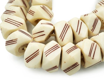 May include: A strand of white and brown ceramic beads with a geometric shape and red stripes. The beads are strung together on a cord.