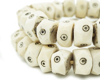 May include: A white bone bracelet with black eye-like designs on each bead.
