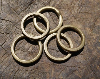 May include: A collection of five brass rings, each with a circular shape and a slightly textured surface. The rings are arranged in a loose pile, with some overlapping. The warm, golden color of the brass contrasts with the dark, wooden background.