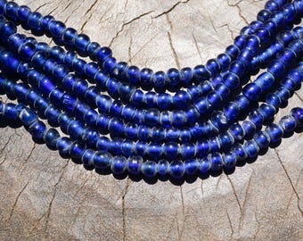 May include: A multi-strand necklace composed of small, round, translucent cobalt blue glass beads. The beads are strung in several parallel rows, creating a layered effect with a consistent deep blue color and a smooth, reflective surface finish.
