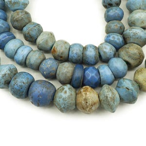 May include: A strand of blue glass beads with a distressed, aged look. The beads are round and have a slightly irregular shape.