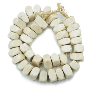May include: A strand of off-white, geometric beads. Each bead is a rectangular shape with beveled edges. The beads are strung together with a natural fiber cord, creating a necklace or bracelet.