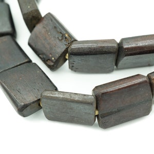 May include: A close-up of a dark brown wooden beaded necklace. The beads are rectangular and have a smooth, polished finish.