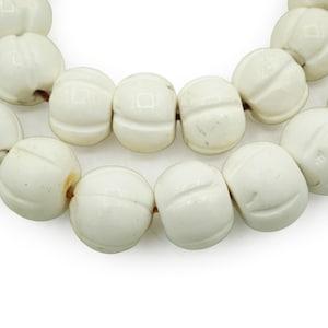 Peut inclure: Un collier de perles en céramique blanche avec un motif sculpté. Les perles sont rondes et ont une finition lisse et polie.