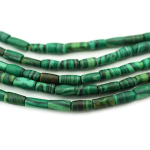 May include: Close-up of several strands of green malachite beads. The beads are cylindrical with dark green and black stripes. The beads are strung together, creating a textured and natural look. The background is white.