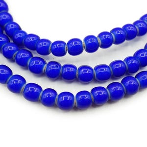 May include: Close-up of three strands of vibrant blue glass beads. Each bead is a rounded shape with a slightly flattened surface. The beads are strung together, creating a necklace or bracelet component. The background is white, highlighting the beads' color.