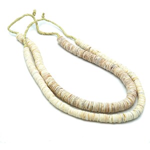 Op de afbeelding: Een dubbele ketting van witte en beige schelp kralen. De ketting is gebonden met een natuurlijk vezelkoord.