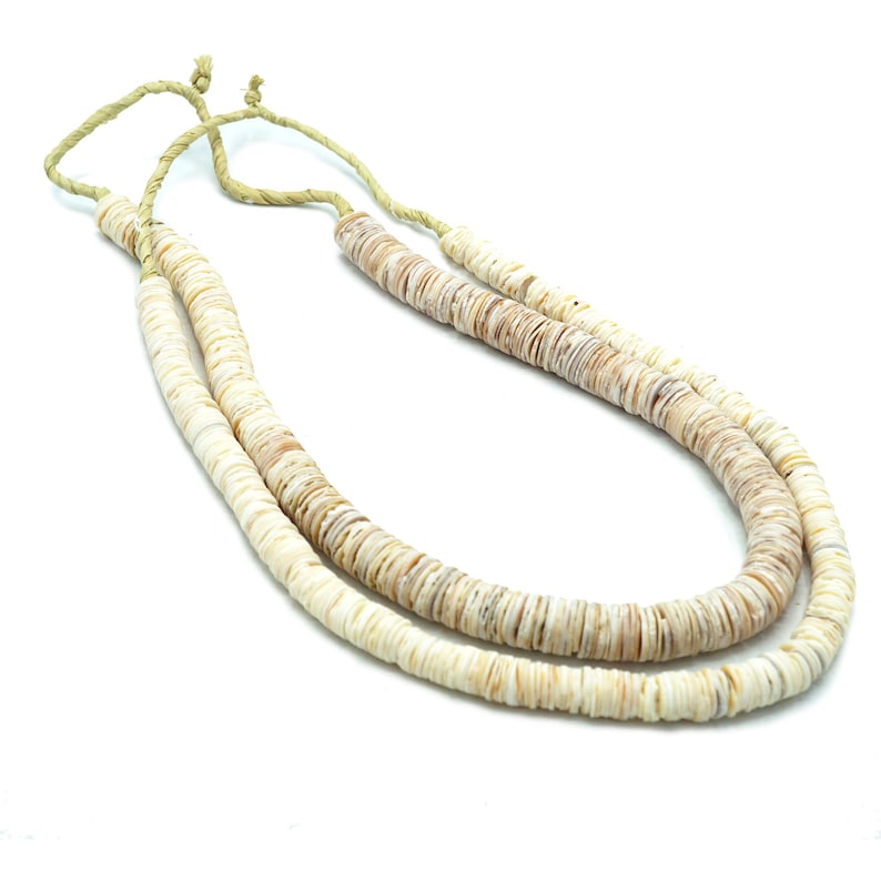 Op de afbeelding: Een dubbele ketting van witte en beige schelp kralen. De ketting is gebonden met een natuurlijk vezelkoord.