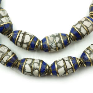 May include: Close-up of a necklace featuring barrel-shaped beads. The beads have a mosaic pattern of white and gray pieces, accented with blue and gold-colored metal bands. The necklace is displayed against a white background.