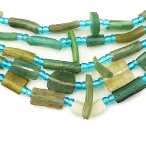 May include: A multi-strand necklace made of green and blue glass beads. The beads are of various shapes and sizes, including long cylinders, squares, and irregular shapes. The necklace is strung on a thin blue cord.