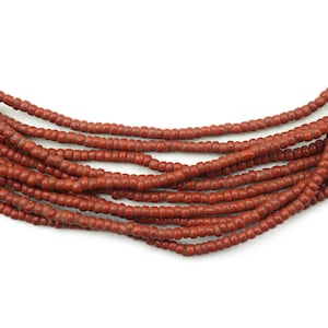 May include: Strands of small, round, reddish-brown beads. The beads are strung together, creating multiple layers. The beads have a matte finish and appear to be made of a natural material. The background is plain white.