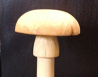 May include: A wooden mushroom sculpture with a light beige color. The mushroom has a rounded cap and a long, slender stem. The sculpture is made of wood and has a natural finish.