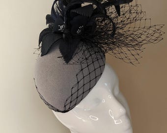 Grey and black teardrop shape will felt hat. Decorated with flowers, feathers and veiling. Great for Cheltenham festival and winter weddings
