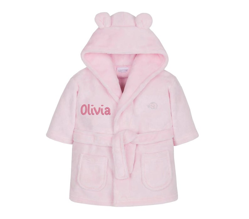 May include: Pink hooded bathrobe with bear ears and a personalized embroidered name "Olivia" on the front.
