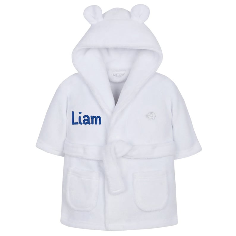 May include: White hooded robe with a blue embroidered name "Liam" and a small elephant design. The robe has a tie belt and pockets.