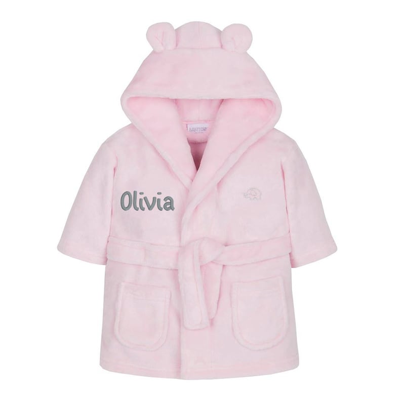 May include: Pink hooded robe with a tie belt and two pockets. The robe has a gray embroidered elephant on the front and the name "Olivia" embroidered on the left side.