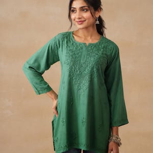 Op de afbeelding: Een smaragdgroene tuniek met lange mouwen, een ronde halslijn met een kleine split en ingewikkeld tonaal bloemenborduursel op de borst en verspreid over het lichaam. Het kledingstuk heeft een rechte zoom met zijsplitten en lange mouwen.