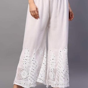 May include: White palazzo pants with a white embroidered design and mirror embellishments. The pants have a wide leg and a flared hem.
