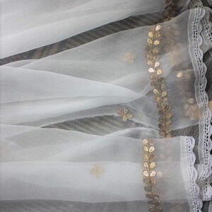 May include: White sheer fabric with a gold leaf and flower design trim. The fabric has a delicate, flowing texture.