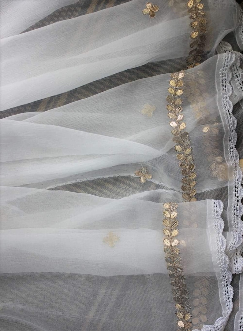 May include: White sheer fabric with a gold leaf and flower design trim. The fabric has a delicate, flowing texture.