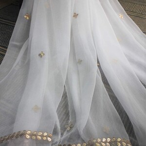 May include: White sheer scarf with gold embroidered floral designs and a gold leaf trim.