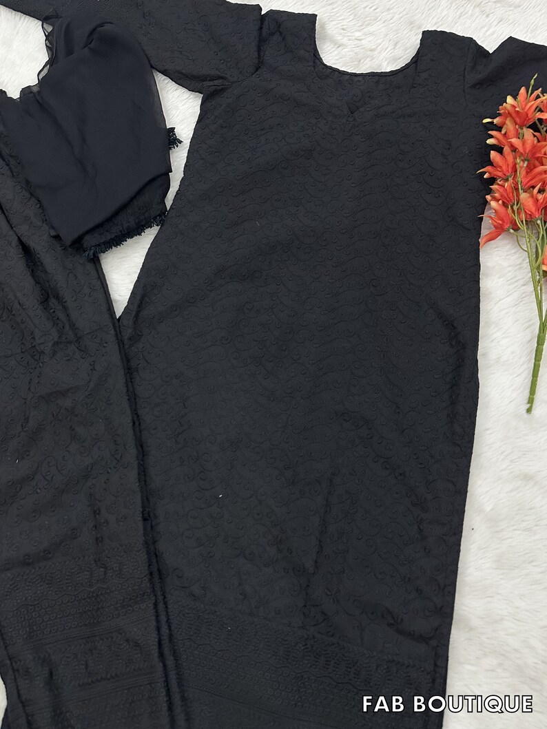 May include: Black embroidered three-piece suit with long sleeves and a round neckline. The suit includes a long top, pants, and a dupatta.