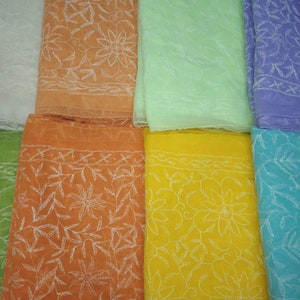 Op de afbeelding: Een assortiment van acht transparante stoffen in verschillende kleuren, waaronder wit, oranje, lichtgroen, geel, blauw en paars. Elke sjaal heeft een delicaat wit geborduurd bloemenpatroon.