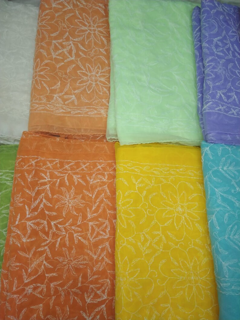 Op de afbeelding: Een assortiment van acht transparante stoffen in verschillende kleuren, waaronder wit, oranje, lichtgroen, geel, blauw en paars. Elke sjaal heeft een delicaat wit geborduurd bloemenpatroon.