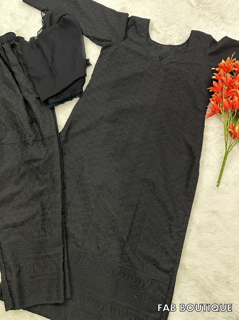 May include: A black embroidered three-piece suit with a long-sleeved top, pants, and a dupatta. The suit has a delicate floral pattern.