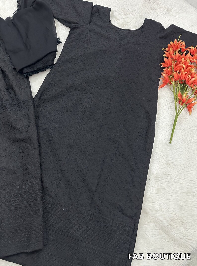 May include: Black embroidered dress with a matching dupatta. The dress has a round neckline and three-quarter sleeves. The dupatta is sheer and has a lace trim.