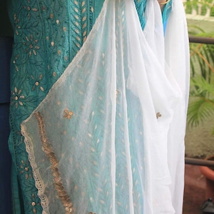 May include: A teal blue embroidered kurta with gold detailing and a white sheer dupatta with gold trim.