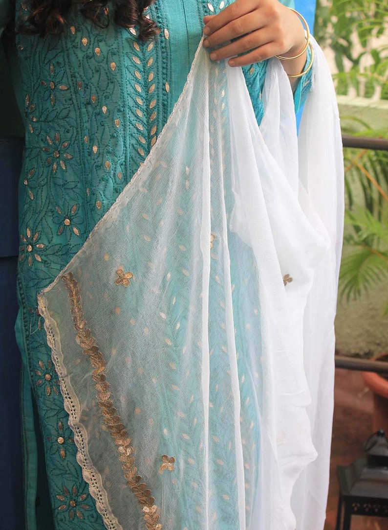 May include: A teal blue embroidered kurta with gold detailing and a white sheer dupatta with gold trim.