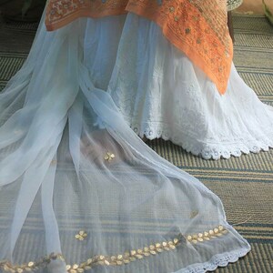 May include: A white sheer fabric with gold leaf embroidery and a white lace trim. The fabric is draped over a white skirt with lace trim.