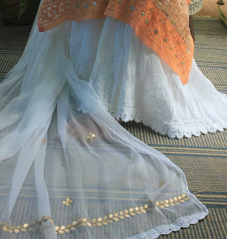 May include: A white sheer fabric with gold leaf embroidery and a white lace trim. The fabric is draped over a white skirt with lace trim.