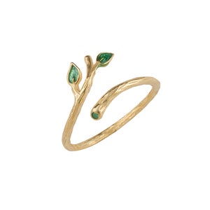 Puede incluir: Un anillo de oro con un diseño de rama y dos hojas verdes. El anillo es ajustable y se puede usar en cualquier dedo.