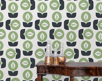 May include: A white wall with a repeating pattern of green and black stylized leaf designs. A dark brown wooden table with two clear glass bottles and a gold metal bottle stopper sits in front of the wall.