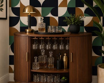 May include: A curved wooden bar cabinet with vertical slats, gold-toned legs, and handles. The interior features a hanging rack for stemware, two shelves holding glass decanters, tumblers, a gold cocktail shaker, and a black utensil holder.