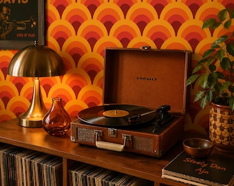 May include: A brown suitcase-style portable record player with the Crosley logo on the interior lid. The turntable features a black platter with a vinyl record, a tone arm, and a front-facing handle, resting on a wooden shelf filled with records.