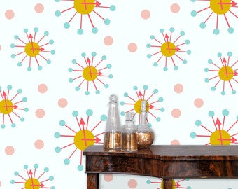 May include: A white background with a repeating pattern of pink circles and blue and red stylized clocks. Three clear glass bottles with gold accents are on a dark brown wooden table in front of the wall.