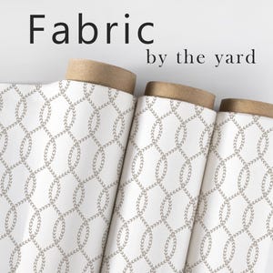 May include: Rolled fabric with a white background and a repeating pattern of interconnected olive-green leaf-like shapes. The fabric is labeled "Fabric by the yard" in black text.