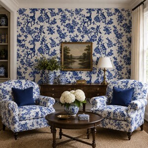 Puede incluir: Un sal&oacute;n acogedor con sillones y papel pintado a juego con estampado floral azul y blanco. Una mesa de centro de madera oscura y un mueble de madera est&aacute;n en el centro. Tambi&eacute;n se ve una pintura de paisaje y una l&aacute;mpara de mesa.