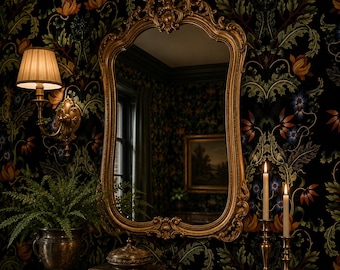May include: A large, ornate gold-toned wall mirror with a curved, decorative frame featuring intricate scrollwork. The mirror is mounted on a dark wall covered in a floral wallpaper pattern with orange, blue, and green botanical motifs.