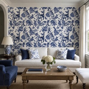 Puede incluir: Un sal&oacute;n con un sof&aacute; blanco, cojines azul marino y cojines con estampado floral. El papel pintado es un dise&ntilde;o toile de Jouy azul y blanco con gatos, flores y mariposas. Una mesa de centro de madera exhibe un jarr&oacute;n con flores blancas y un cuenco decorativo.