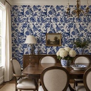 Puede incluir: Un comedor con papel pintado floral azul y blanco con ciervos y motivos florales. Una mesa de madera est&aacute; decorada con un jarr&oacute;n de flores blancas y un plato azul y blanco. Tambi&eacute;n se ven un aparador de madera y una l&aacute;mpara de ara&ntilde;a.