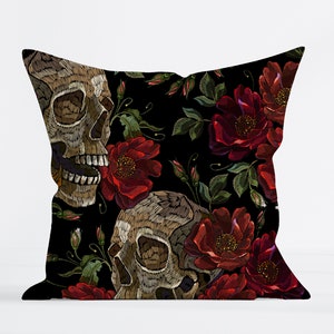 Puede incluir: Almohada negra con rosas rojas bordadas y dos calaveras blancas. Las calaveras están detalladas con cuencas de los ojos, narices y dientes.